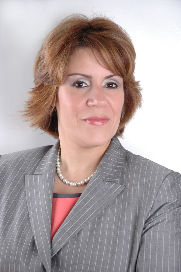 Eine selbstbewusste Frau in einem marineblauen Businessanzug mit einem weißen Hemd und einer gemusterten Krawatte posiert aufrecht gegen einen weißen Hintergrund, ihr direkter Blick und ihr professionelles Auftreten vermitteln Stärke und Entschlossenheit.