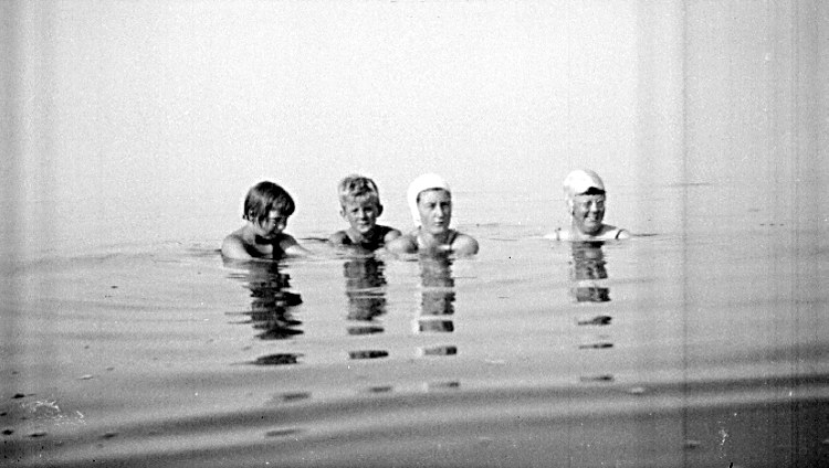 Schwarzes und weißes Foto von vier Kindern, die in einem Pool schwimmen, alle tragen Schwimmkappen.