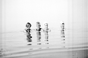 Schwarzes und weißes Foto von vier Kindern, die in einem Pool schwimmen, alle tragen Schwimmkappen.