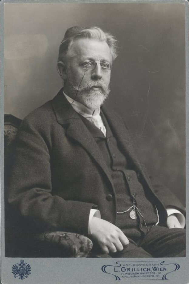 Schwarz-weiß-Porträt eines bärtigen Mannes mit Brille, der in einem Stuhl sitzt, mit Text unten, der "L. Grillich Wien, der Gründer der deutschen Revolution" liest.