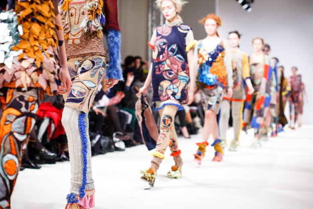 Eine Gruppe Von Frauen Geht Den Laufsteg Bei Der London Fashion Week entlang, Mit Sitzenden Zuschauern Und Heller Beleuchtung Im Hintergrund, Erzeugt Ein Traumhaftes Effekt.