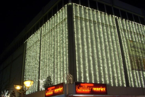 Ein Gebäude in Berlin, Deutschland, geschmückt mit Weihnachtslichtern, umgeben von Bäumen, Laternen und Schildern mit Text, mit dem Himmel im Hintergrund.
