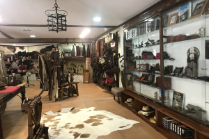 Ein Boutique-Zimmer in Barcelona mit einem Kuhfellteppich, Kleidung an Bügeln, Hüten, Foto Rahmen und verschiedenen Gegenständen in Schränken, beleuchtet von Deckenlampen und einem Kronleuchter.