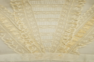 Nahaufnahme eines weißen Kleides mit zarter, detallierter Spitzenverzierung auf einem leichten, luftigen Stoff.