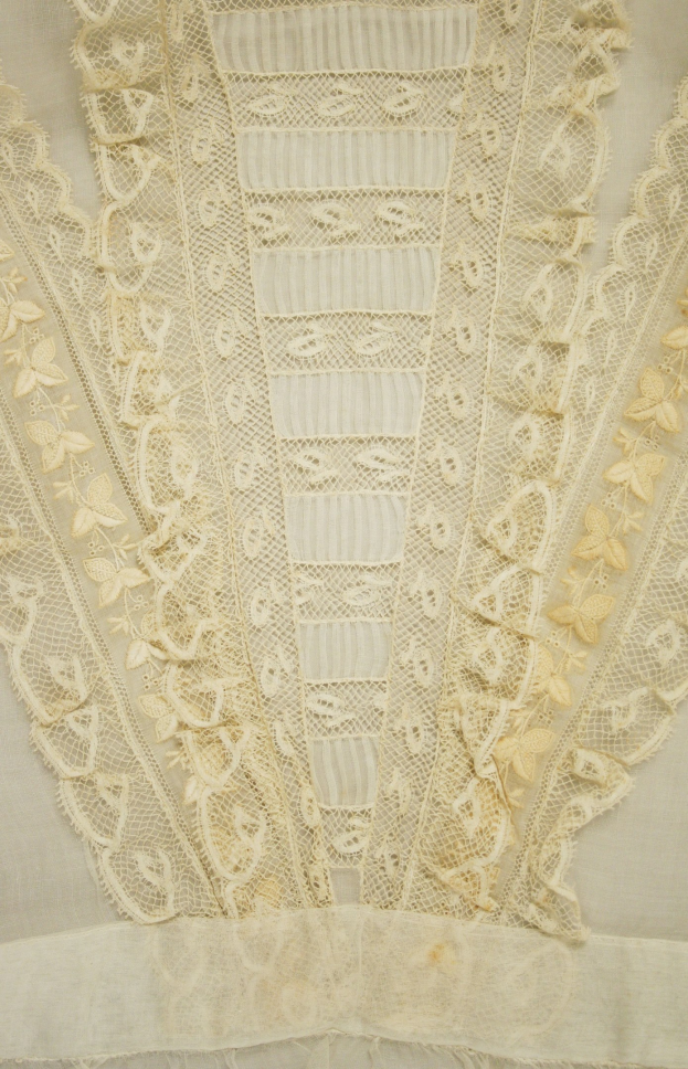 Nahaufnahme eines weißen Kleides mit zarter, detallierter Spitzenverzierung auf einem leichten, luftigen Stoff.