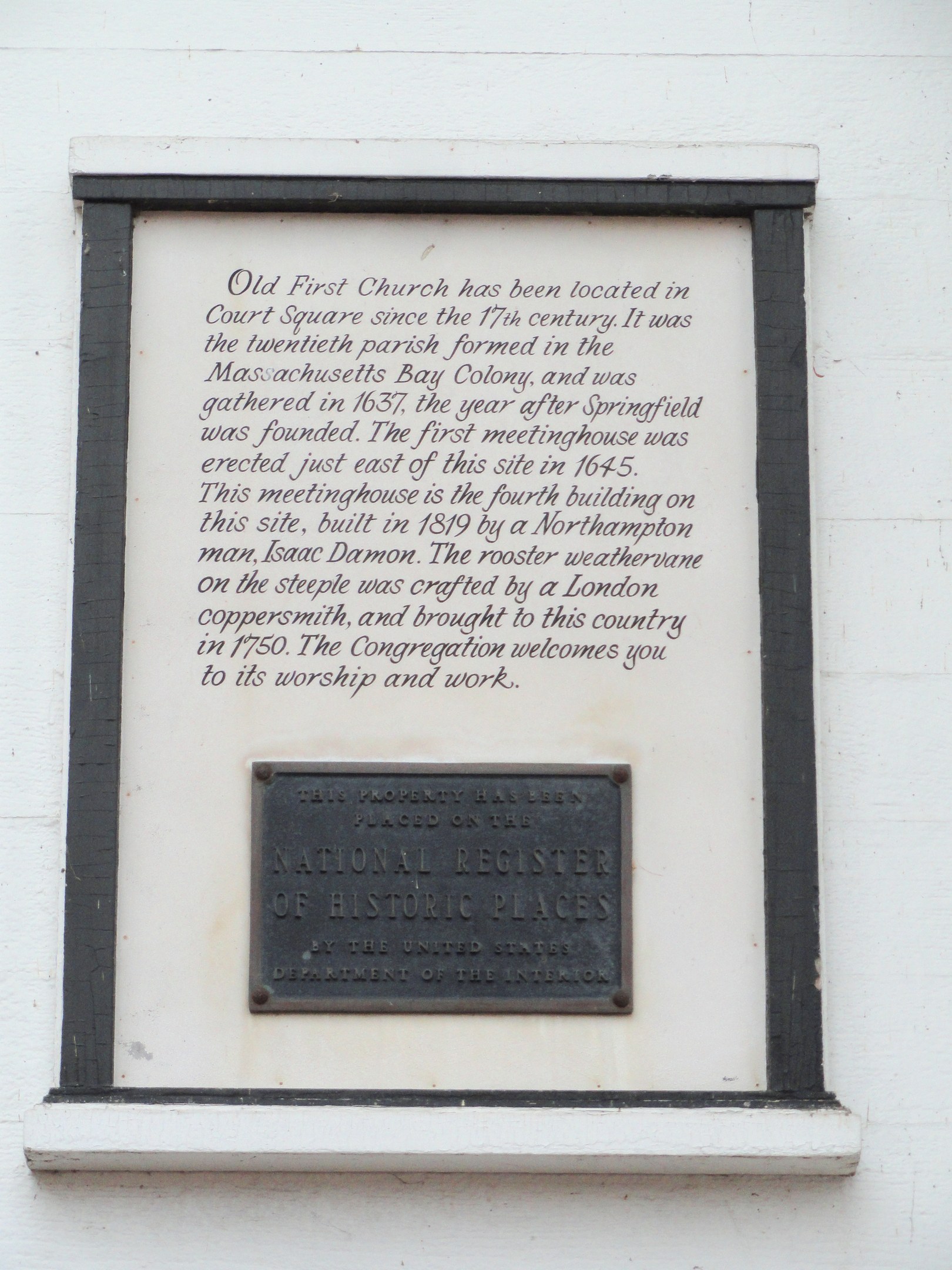 Plaque auf einer Gebäudewand mit der Aufschrift "National Register of Historic Places" in fetter Schrift, innerhalb eines dekorativen Rahmens auf dunklem Material montiert.