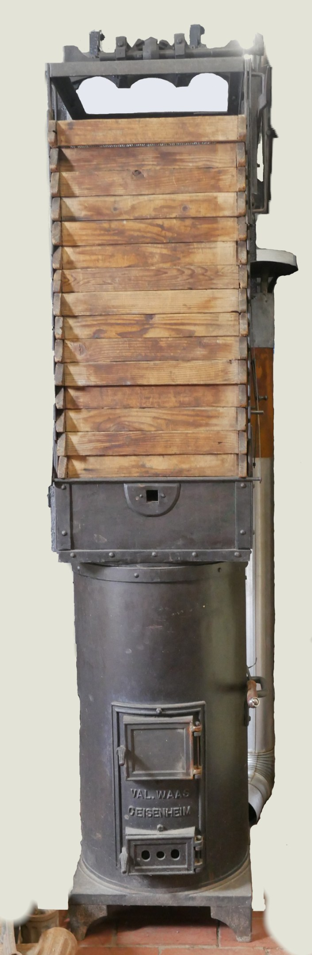 Altmodischer Holzofen mit Metall- und Holzbau, Schornstein, auf einem Ziegelboden gegen eine Wand gestellt.