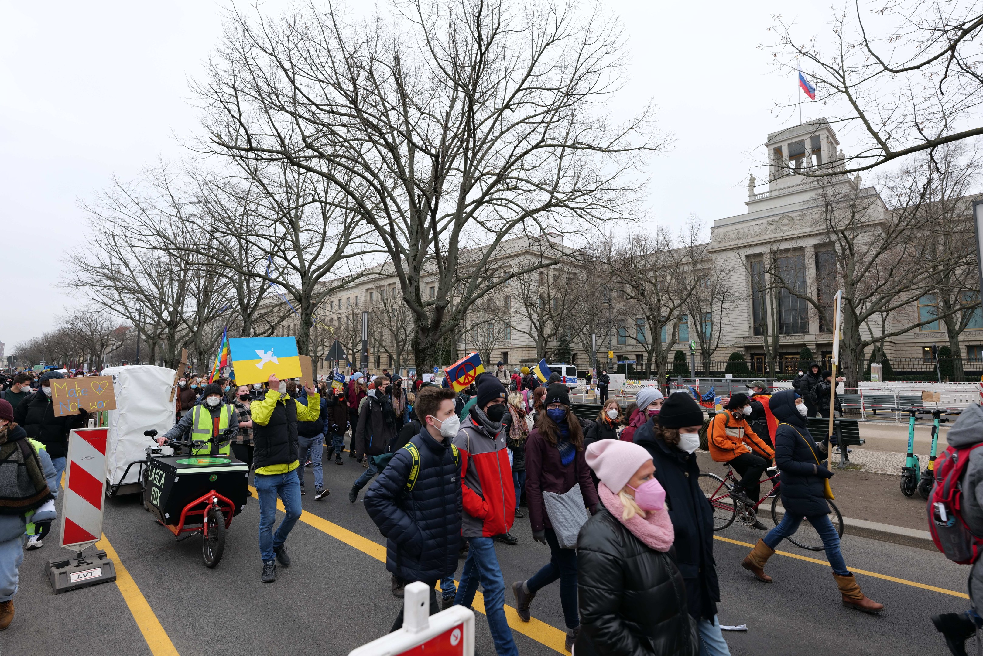 Ein große Protestmarsch mit Menschen, die Schilder halten und Fahrräder fahren, vor einem Gebäude in Washington, D.C. am 21. Januar 2020 unter einem klaren blauen Himmel.