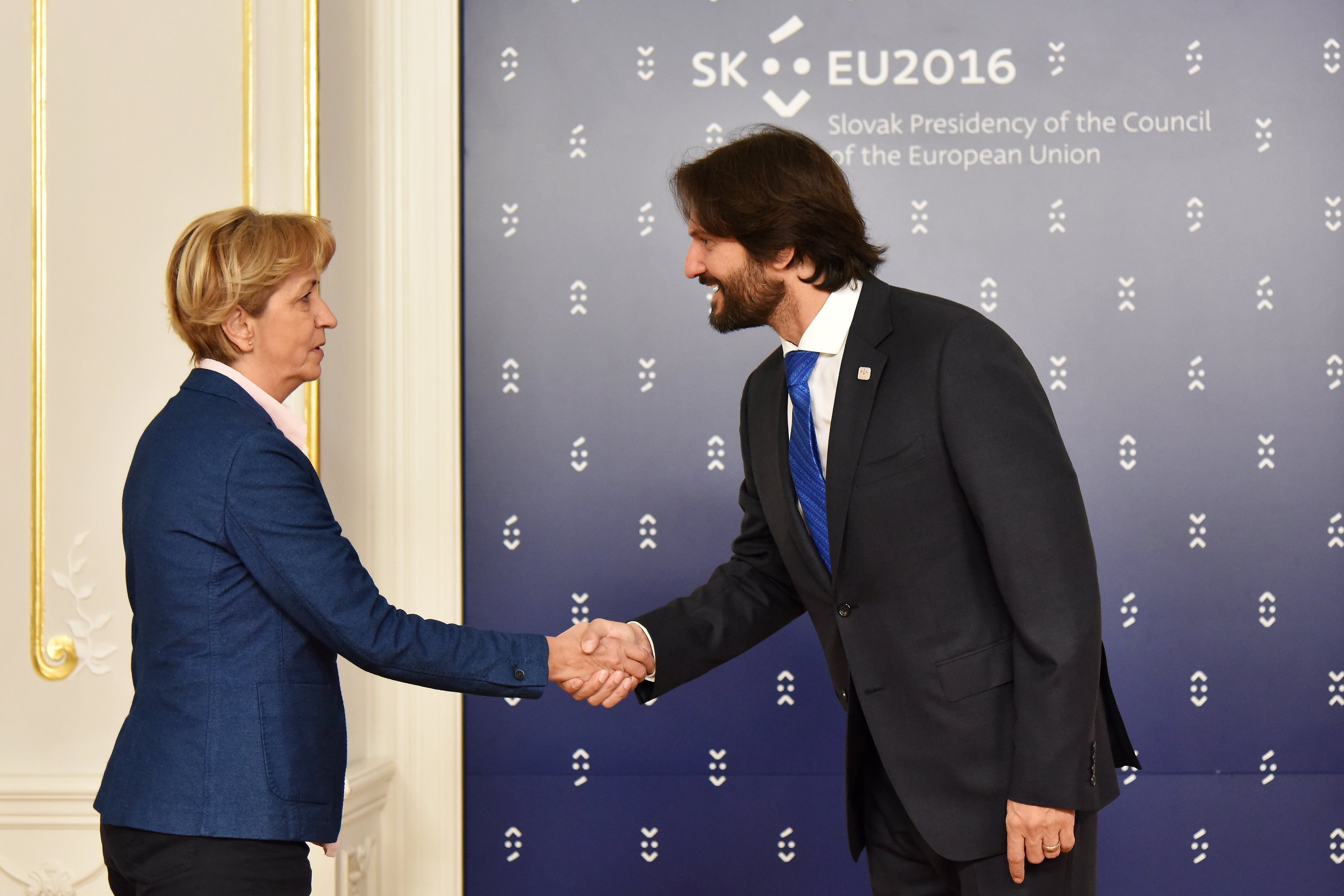 Bundeskanzlerin Angela Merkel und Bundespräsident Joachim Gauck schütteln sich die Hand und lächeln vor einer Wand mit einem "EU-Gipfel"-Schild und einer Tür.