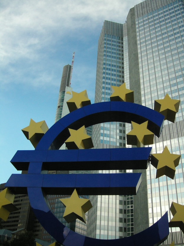 Eurozeichen vor dem Hauptquartier der Europäischen Zentralbank in Frankfurt, Deutschland, mit Bäumen und einem bewölkten Himmel.