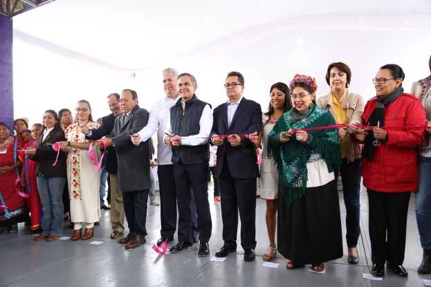 Eine Gruppe von Menschen bei einer Scherenschnittzeremonie, die Schere haltend, vor einer Menge mit Papieren auf dem Boden und einem weißen Tuch im Hintergrund.