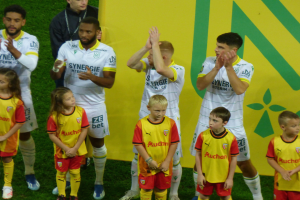 Eine Gruppe von Fußballspielern in Uniformen klatscht feierlich auf einem Ligue-1-Feld mit einer "Ligue-1"-Platte im Hintergrund.