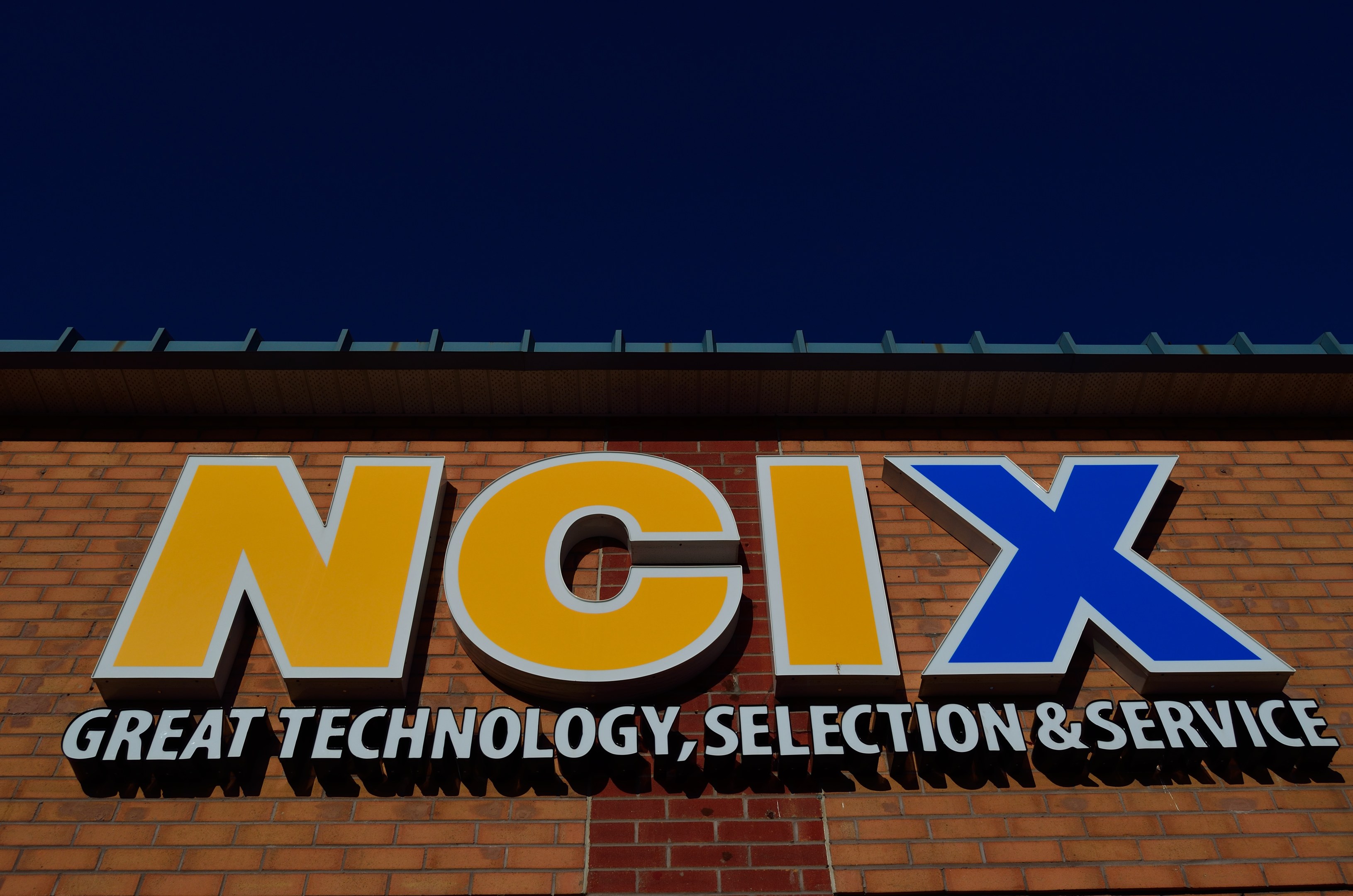 Brick building with a sign reading "NCIX Great Technology, Selection & Service" under a clear blue sky.