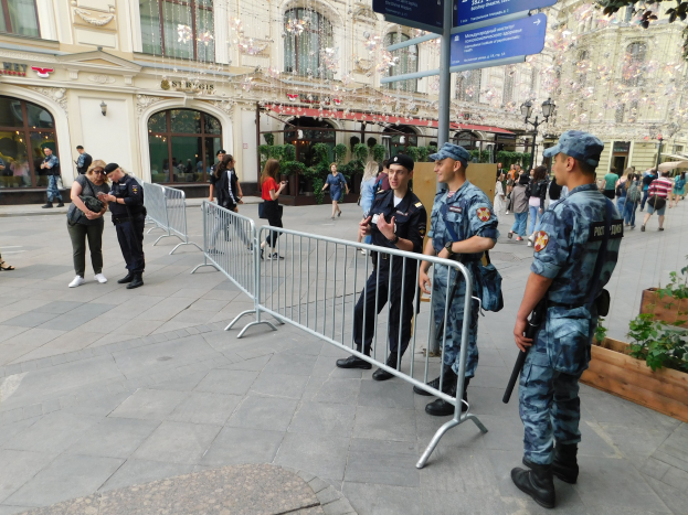 Polizeibeamte in Uniform vor einer Menge, einige mit Waffen, mit Absperrungen und Schildern im Vordergrund, vor Gebäuden und Grün in Wien während einer Anti-Terror-Operation.