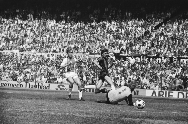 Schwarzes Foto von Männern, die auf einem Feld Fußball spielen, mit Zuschauern im Hintergrund und einer Bundesliga 1978-79 Ajax 1-1 Hannover 96 Fahne.