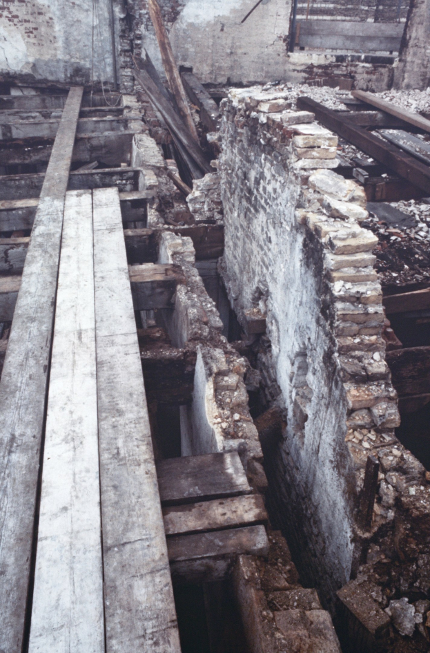Abriss eines alten Gebäudes mit verstreuten Holzplanken und Steinen im Vordergrund und einer remaining Wand im Hintergrund.