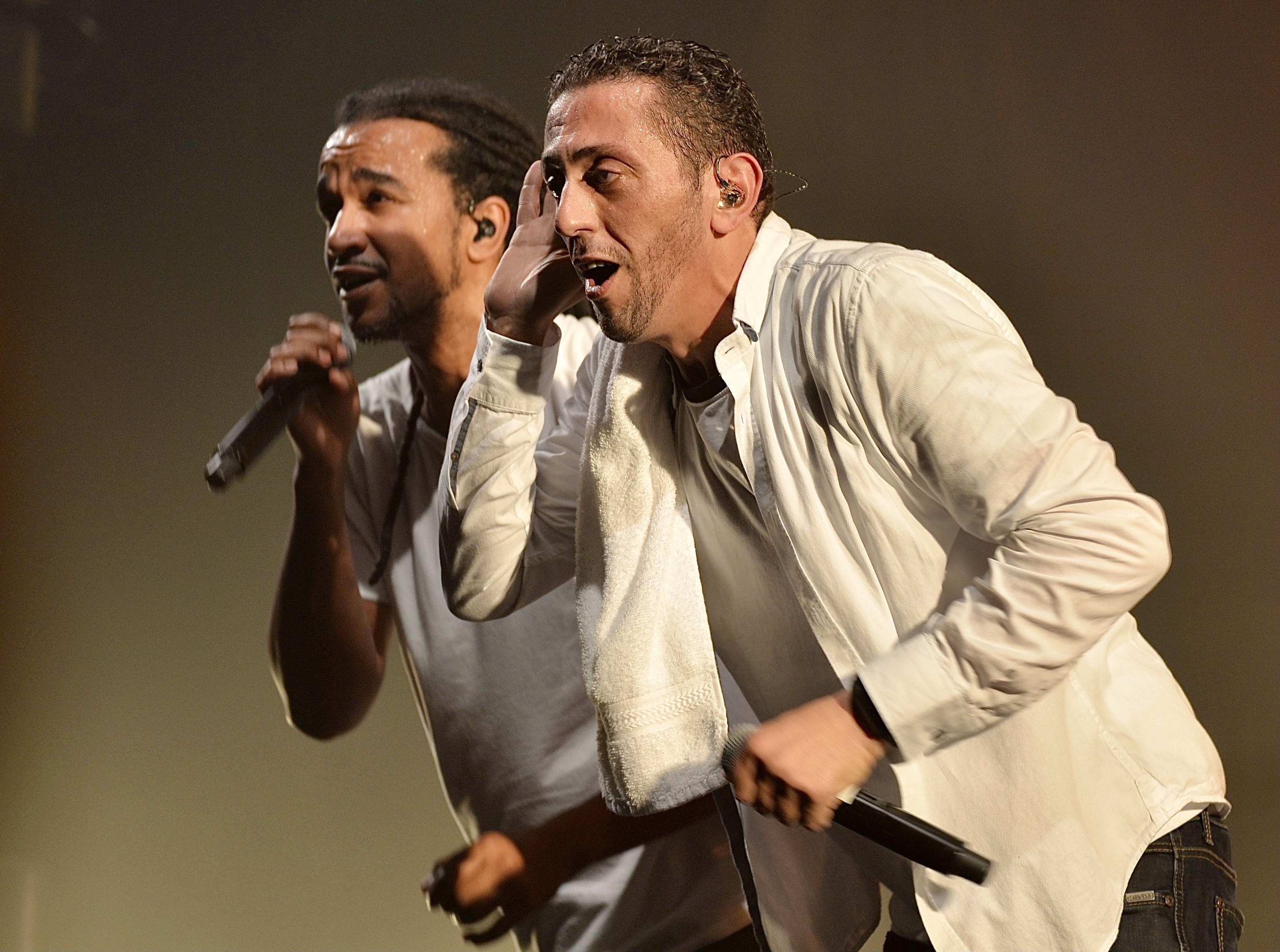 Zwei Männer in legerer Kleidung performen auf der Bühne nebeneinander, jeder hält ein Mikrofon in der Hand.