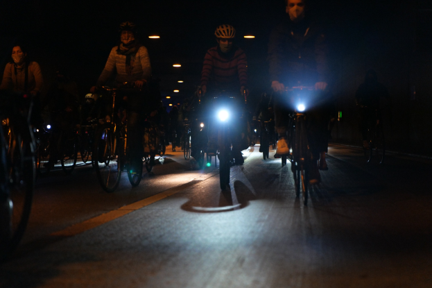 Eine Gruppe von Menschen, die nachts mit Fahrrädern eine Stadtstraße hinunterfahren, alle tragen Helme.