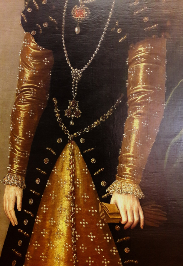 Bild einer Frau in goldenem Kleid mit hohem Ausschnitt und langen Ärmeln, die eine Tasche hält, mit einem Dutt und seitlichem Blick.