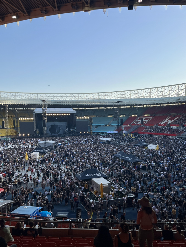 Große Menschenmenge auf Tribünen und im Stehen in einem Stadion mit Zelten, Geländern und Scheinwerfern, was auf ein Konzert in der O2 Arena in London hindeutet.