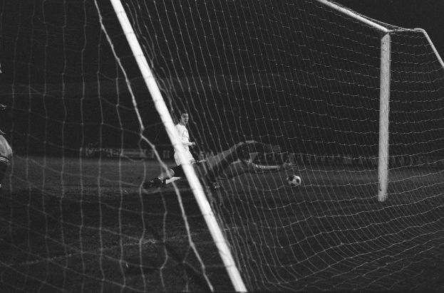 Ein Fussballspieler in einem Schwarz-Weiß-Foto hält einen Ball und steht vor einem Tor.