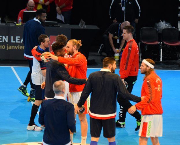 Mannengruppe auf einem Futsal-Platz mit Bällen, die vor einem Tisch mit Flaschen, Laptops und einer Tafel mit Text feiern.