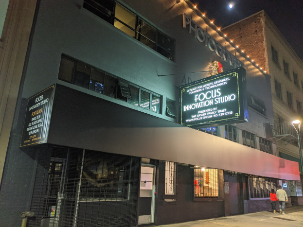 Eine nächtliche Aufnahme des Focus Innovation Studio in New York City, mit beleuchteten Gebäuden, Passanten auf dem Gehweg und sichtbarem Himmel im Hintergrund.