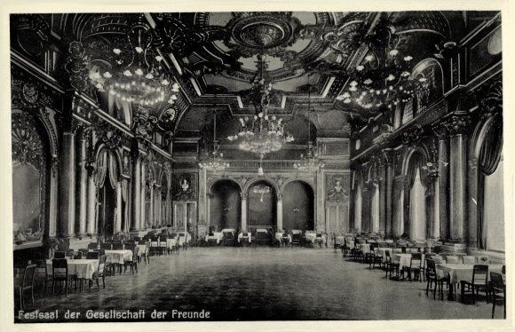 Schwarz-weiß-Foto eines großen Raums mit Tischen, Stühlen, Säulen, Bögen und Kronleuchtern, beschriftet mit "Festival der Gesellschaft der Freunde, Berlin" unten.