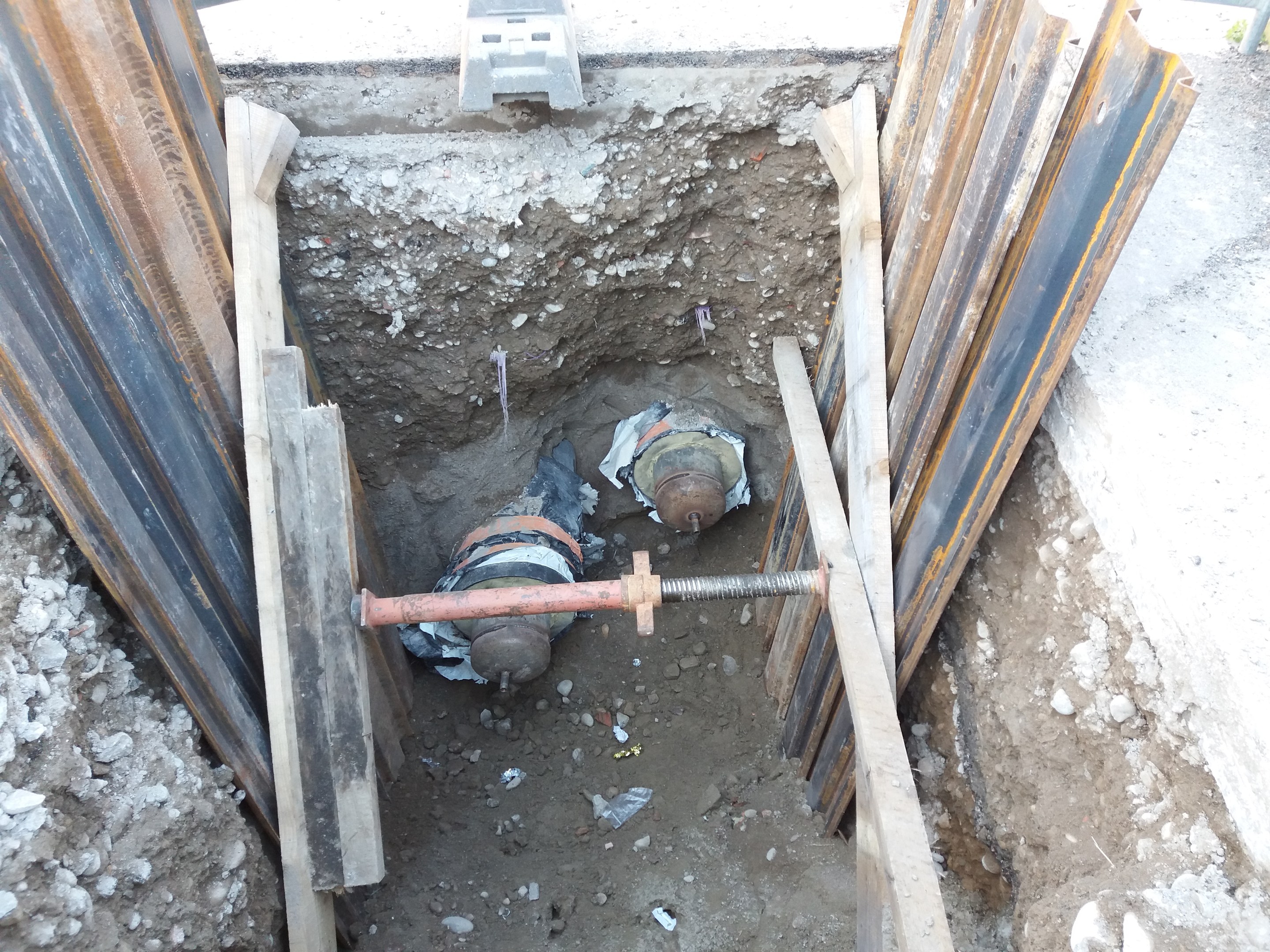 Großer Krater auf einer Baustelle umgeben von Metallstäben und Steinen, mit einem Fahrzeug oben, das laufende Bauarbeiten anzeigt.