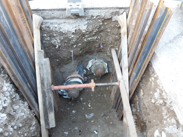 Großer Krater auf einer Baustelle umgeben von Metallstäben und Steinen, mit einem Fahrzeug oben, das laufende Bauarbeiten anzeigt.