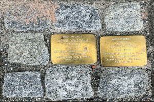 Drei Messingplaketten, die in einen Kopfsteinpflasterweg eingelassen sind und jeweils mit Gedenktext beschriftet sind.