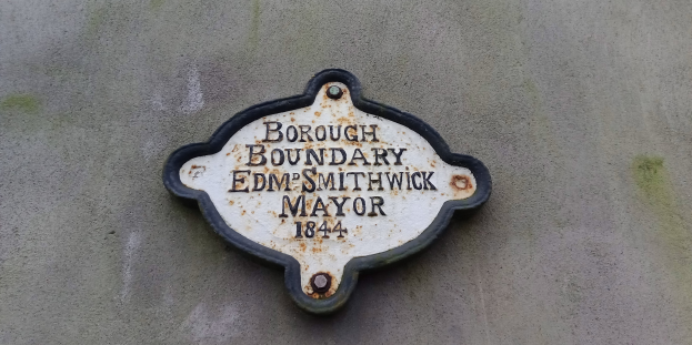 Eine schwarze Metalltafel mit weißer Schrift, die "Stadtgrenze Edm Smithwick Bürgermeister" trägt, an einem Gebäude angebracht.