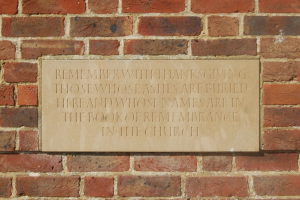 Eine Backsteinwand mit einer Plakette, auf der steht: "Erinnere dich mit Dankbarkeit an diejenigen, deren Asche hier begraben ist und deren Namen im Buch der Erinnerung in der Kirche stehen."