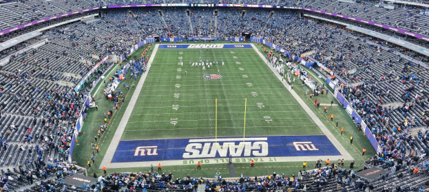 Ein Fußballstadion voller Zuschauer, Spieler, Pfosten und Schilder mit Text, umgeben von Reihen von Stühlen.