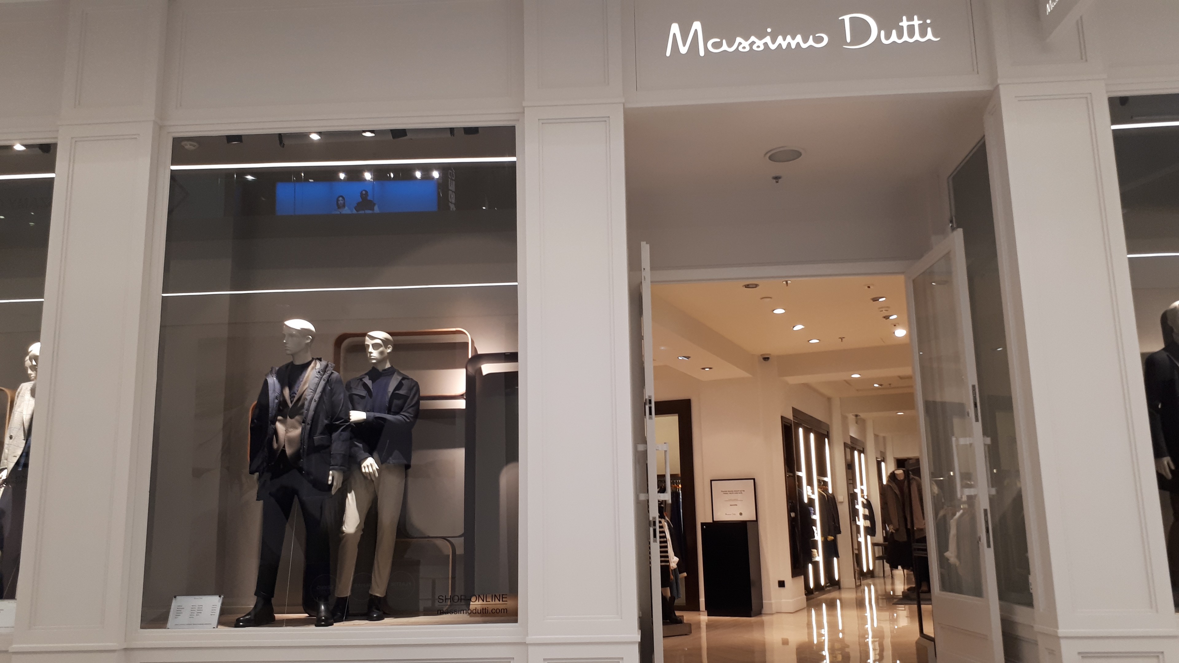 Ein Massimo Dutti Geschäft in Mailand, Italien, mit Schaufensterpuppen in modischen Auslagen, Texttafeln, Deckenleuchten und sichtbarem Bodenbelag.