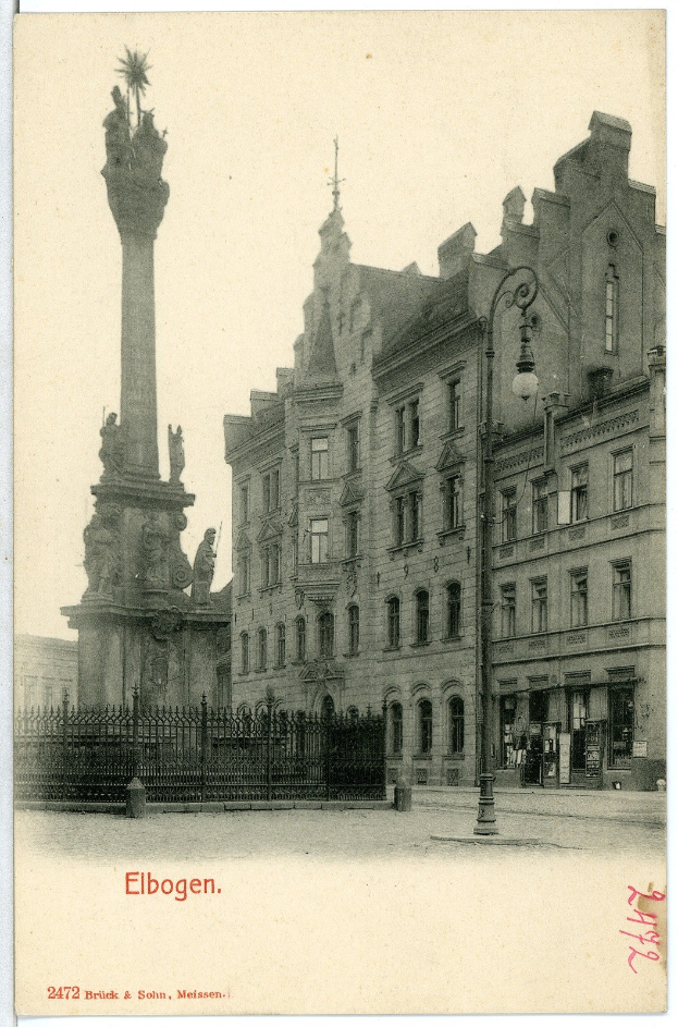 Schwarz-weiß-Foto eines Stadtplatzes mit einem zentralen Denkmal, umgeben von Gebäuden, Straßenlaternen, Lampen und Gittern unter einem klaren Himmel, mit Text unten.