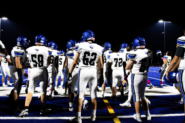 Eine Gruppe von Fußballspielern in Helmen und Stiefeln auf einem Feld unter Flutlicht.