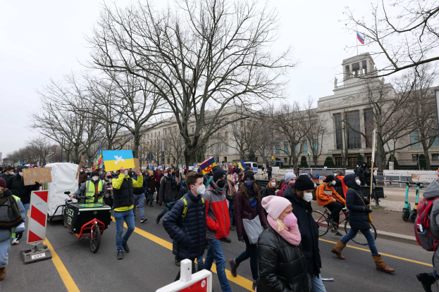 Eine große Gruppe von Menschen marschiert auf einer Straße in Washington, D.C. am 21. Januar 2020 mit Schildern und Bannern, einige fahren Fahrräder, mit Bäumen und einem klaren blauen Himmel im Hintergrund.