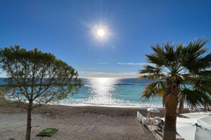 Ein sonniger Strand mit Palmen, Sonnenschirmen und üppiger Vegetation an der französischen Riviera unter einem strahlend blauen Himmel.