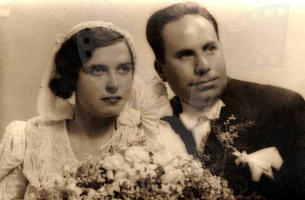 Ein Schwarz-Weiß-Foto eines strahlenden Mannes und einer Frau an ihrem Hochzeitstag, die Frau in einem weißen Kleid mit einem Blumenstrauß, der Mann steht neben ihr.