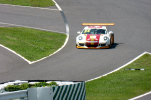 Ein Porsche 911 GT3 RSR auf der Nürburgring 24 Stunden Rennstrecke, umgeben von grünem Gras und einem Geländer, mit dem Auto in hellen Farben und einem eleganten Design.