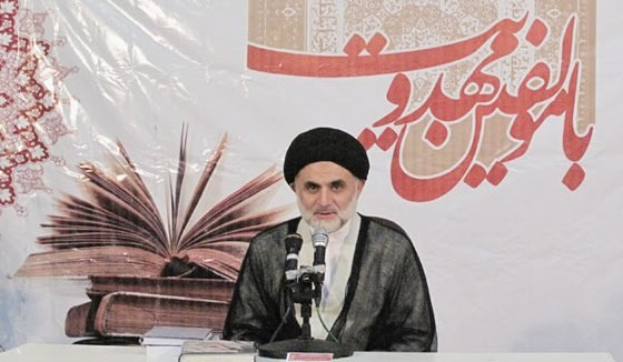 Ayatollah Ali Khamenei, Oberster Führer von Iran, sitzend mit Büchern und Mikrofonen auf einem Tisch, hinter einem Banner mit Text und einem Bild eines Buches.