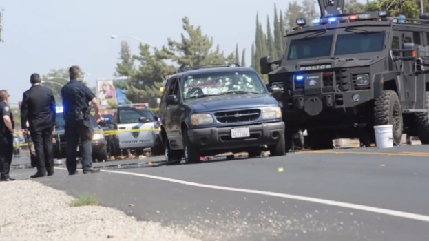 Polizeiauto und Lkw neben einer Gruppe von Menschen, Trümmern und einem Banner an einer Straße in Fresno, Kalifornien.