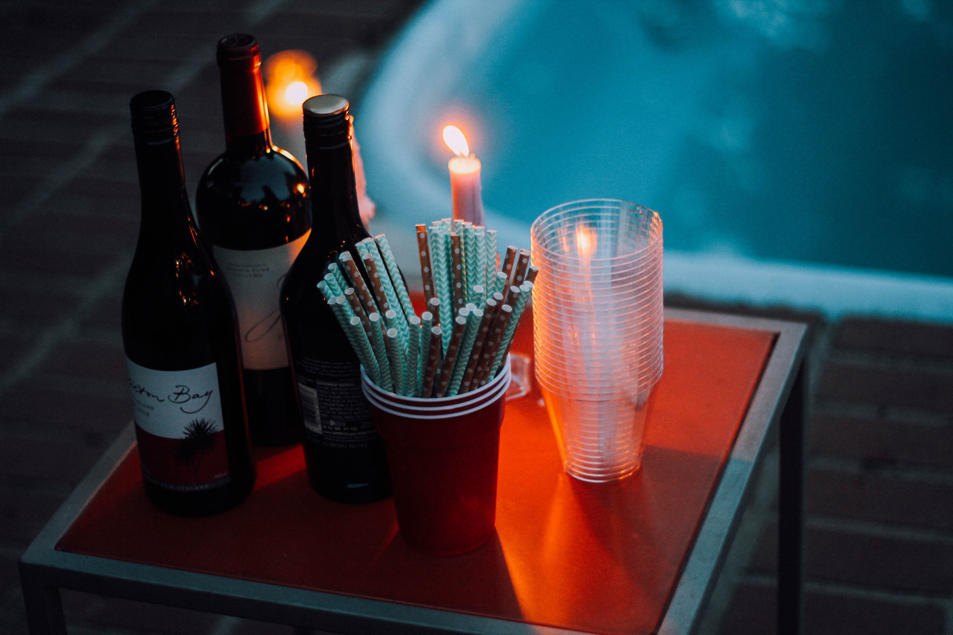 Ein Tisch am Swimmingpool mit zwei Weinflaschen, einer Kerze, Gläsern und Strohhalmen vermittelt ein entspanntes Abendstimmung.