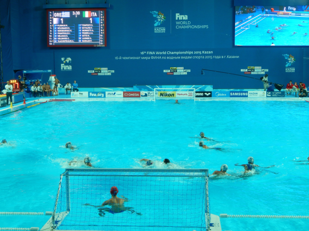Wasserballspieler bei einem Poolwettkampf während der FINA-Weltmeisterschaften 2016 in Kazan, mit Zuschauern auf der linken Seite und einem Anzeigebrett im Hintergrund.