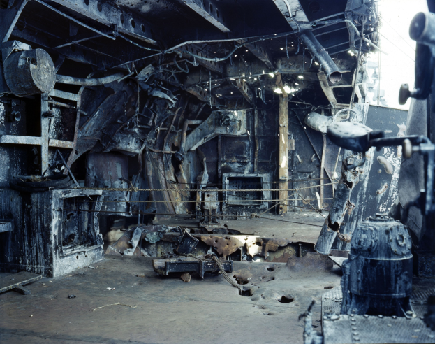 Verkohlte Trümmer und freiliegendes Metallgerüst in einem feuerbeschädigten Gebäude mit sichtbarem Himmel durch die Decke.