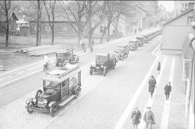 Schwarz-weißes Straßenbild in den 1930er bis 1940er Jahren in Berlin mit Oldtimern, Fußgängern, Gebäuden, Bäumen und einem klaren Himmel.