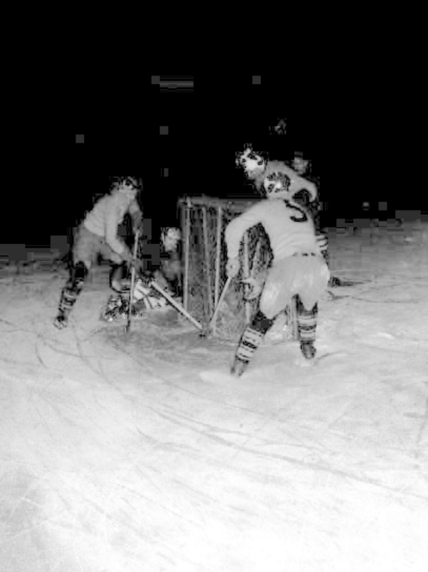 Schwarzes und weißes Foto von Männern, die bei Nacht auf dem Eis Hockey spielen und Helme sowie Stöcke halten.