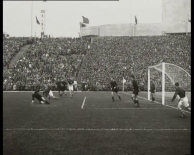 Ein Schwarz-Weiß-Foto eines Fußballspiels im Stadion, mit Spielern auf dem Feld und einem Torpfosten auf der rechten Seite, Zuschauern in den Rängen, Fahnen und einem klaren Himmel, mit Text oben und unten '1958-1958 WM-Finale - Manchester United v Liverpool'.