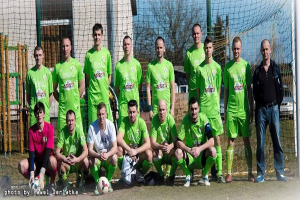 Gruppe von Männern in grünen T-Shirts, die auf einem Fußballfeld neben einem Torpfosten mit einem Ball davor stehen.